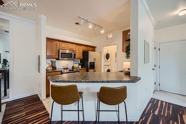 kitchen featuring a kitchen bar, crown molding, stacked washer / dryer, kitchen peninsula, and stainless steel appliances