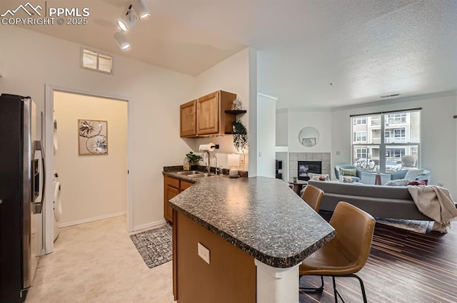 kitchen featuring stainless steel fridge with ice dispenser, sink, a breakfast bar area, a tiled fireplace, and kitchen peninsula