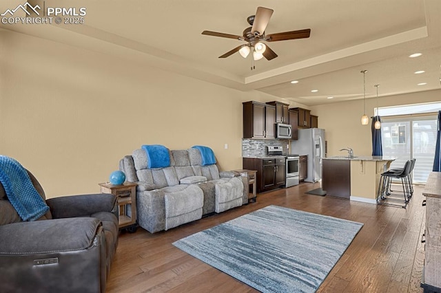 living room featuring dark hardwood / wood-style flooring, sink, a raised ceiling, and ceiling fan