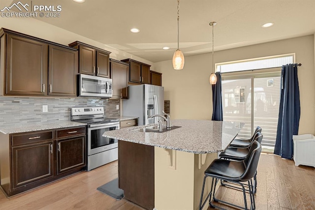 kitchen featuring light stone counters, stainless steel appliances, sink, and a kitchen island with sink