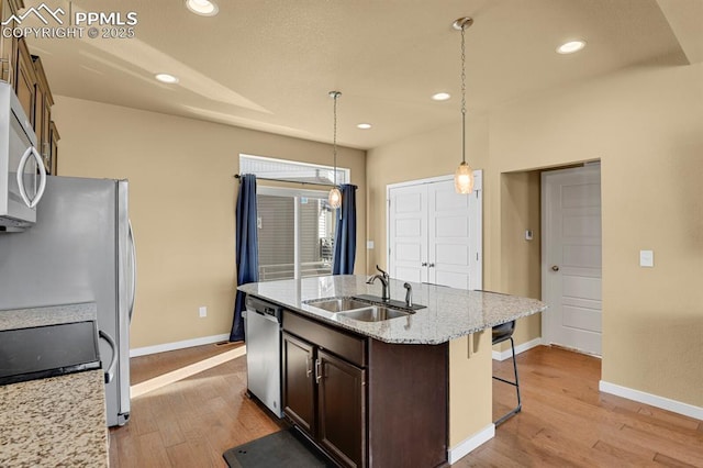 kitchen featuring pendant lighting, sink, light stone counters, stainless steel appliances, and light wood-type flooring