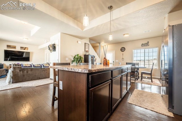 kitchen with a kitchen breakfast bar, stainless steel fridge, decorative light fixtures, a kitchen island, and dark brown cabinetry