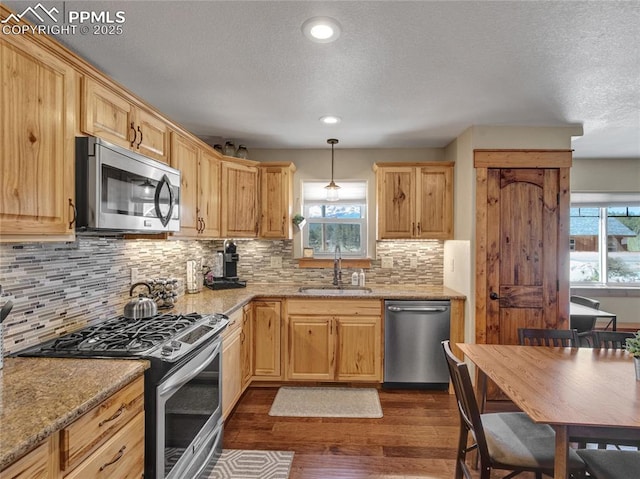 kitchen featuring light stone counters, decorative light fixtures, stainless steel appliances, dark wood-type flooring, and a sink