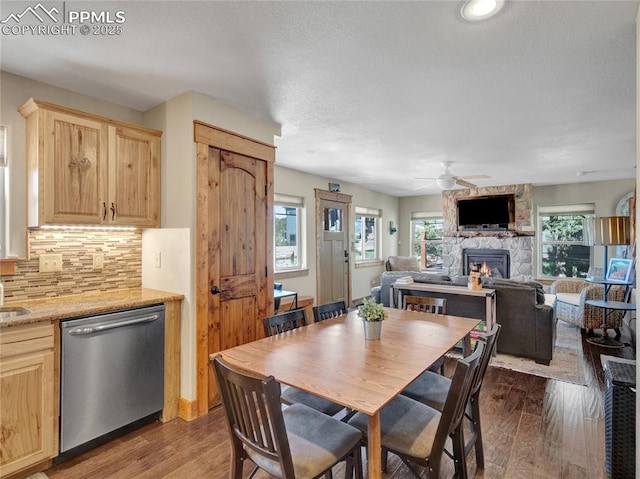 dining area featuring a stone fireplace, dark wood-style flooring, and plenty of natural light