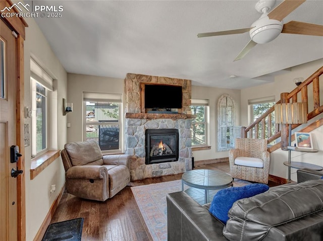 living area featuring a healthy amount of sunlight, a stone fireplace, baseboards, and wood finished floors