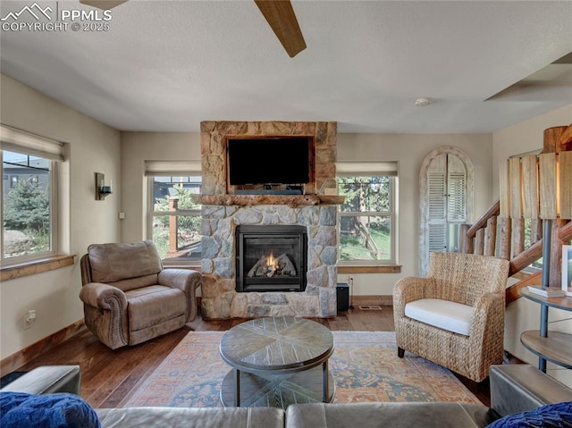 living room featuring a stone fireplace, wood finished floors, visible vents, and baseboards