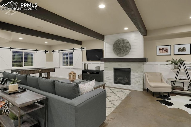 living room with beam ceiling, a fireplace, concrete flooring, and a barn door