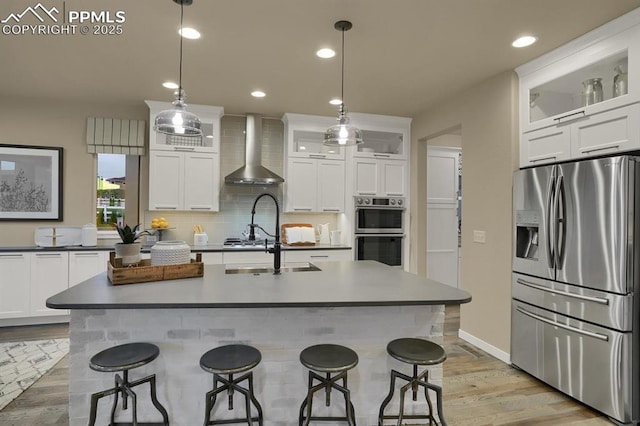 kitchen featuring wall chimney exhaust hood, hanging light fixtures, white cabinets, stainless steel appliances, and backsplash