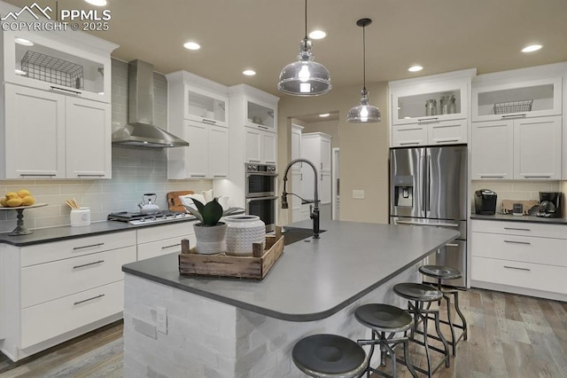 kitchen with stainless steel appliances, white cabinetry, a center island with sink, and wall chimney exhaust hood