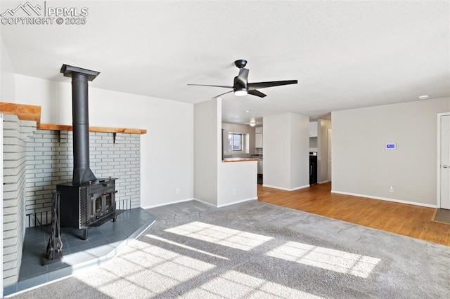 unfurnished living room with ceiling fan, carpet, and a wood stove