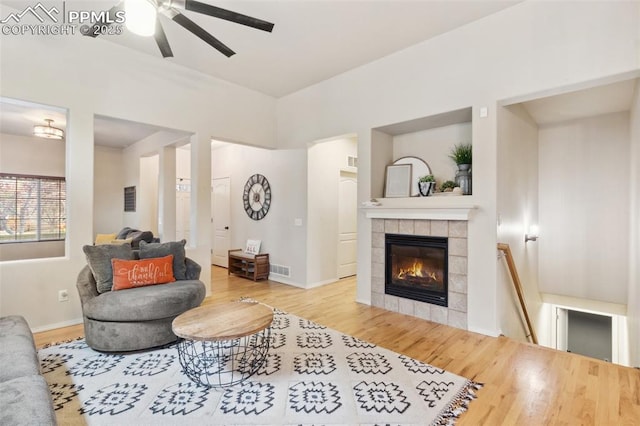 living room with ceiling fan, wood-type flooring, and a tiled fireplace