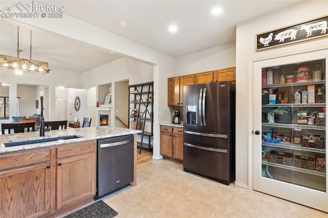 kitchen with sink, light stone counters, appliances with stainless steel finishes, pendant lighting, and a fireplace