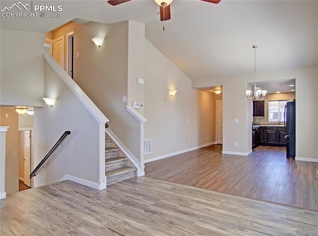 unfurnished living room with hardwood / wood-style flooring, ceiling fan with notable chandelier, and high vaulted ceiling