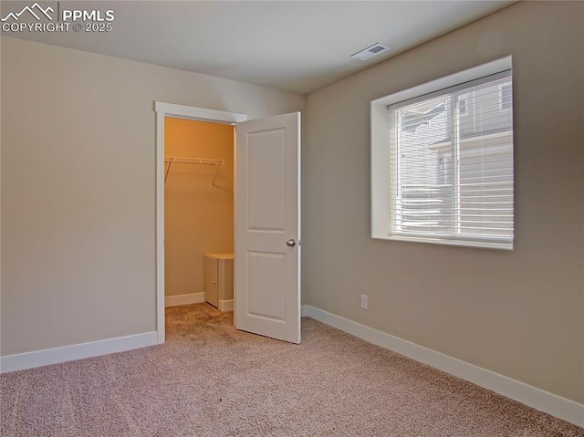 unfurnished bedroom with a closet, a spacious closet, and light carpet