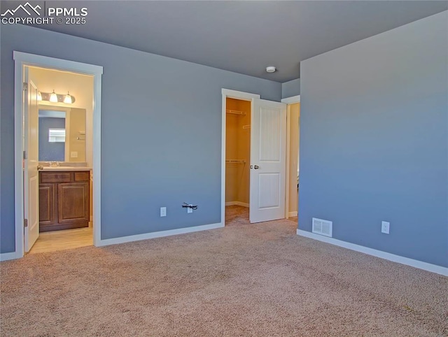 unfurnished bedroom featuring light carpet, sink, a spacious closet, and ensuite bath