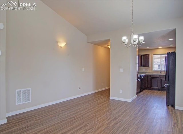 kitchen featuring vaulted ceiling, dark brown cabinets, black refrigerator, and dark wood-type flooring