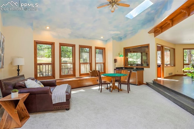 carpeted living room featuring ceiling fan and vaulted ceiling with skylight