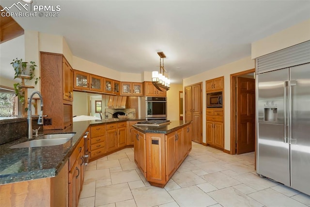 kitchen with sink, built in appliances, hanging light fixtures, kitchen peninsula, and a kitchen island