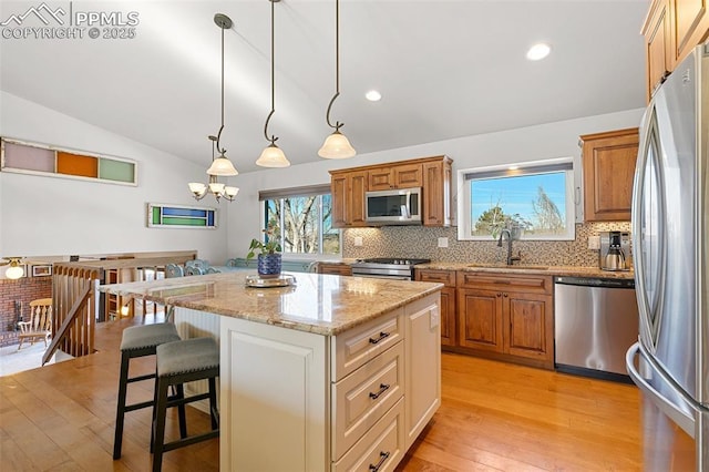 kitchen featuring sink, light stone counters, appliances with stainless steel finishes, a kitchen island, and pendant lighting