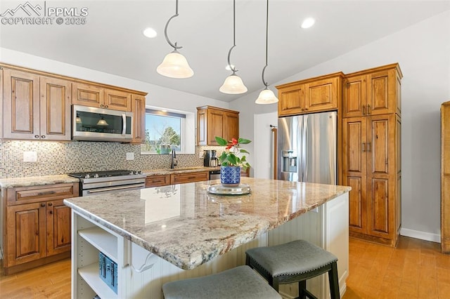 kitchen with light stone counters, appliances with stainless steel finishes, hanging light fixtures, and a kitchen island