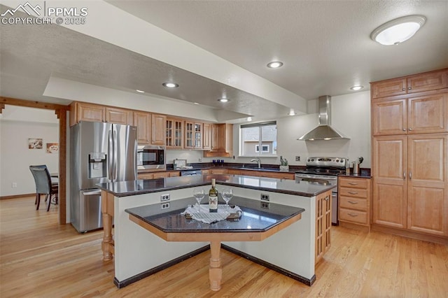 kitchen with wall chimney range hood, sink, a kitchen breakfast bar, stainless steel appliances, and a kitchen island