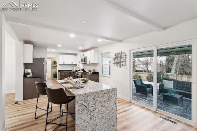 kitchen with appliances with stainless steel finishes, light stone countertops, light hardwood / wood-style floors, white cabinets, and beamed ceiling