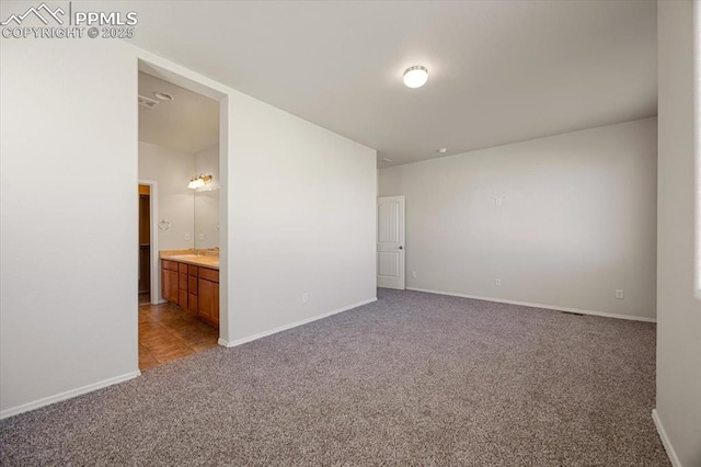 unfurnished bedroom with ensuite bathroom, sink, and light colored carpet