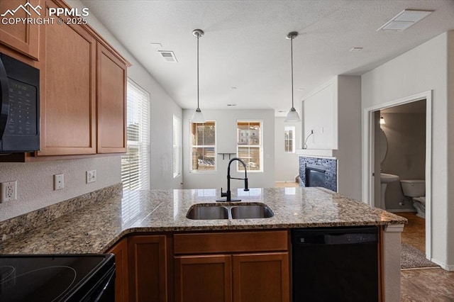 kitchen with decorative light fixtures, black appliances, sink, kitchen peninsula, and light stone countertops