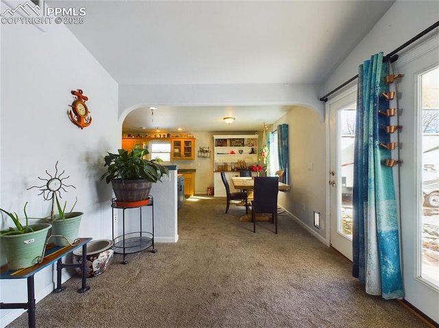 dining space featuring arched walkways, dark carpet, baseboards, and plenty of natural light