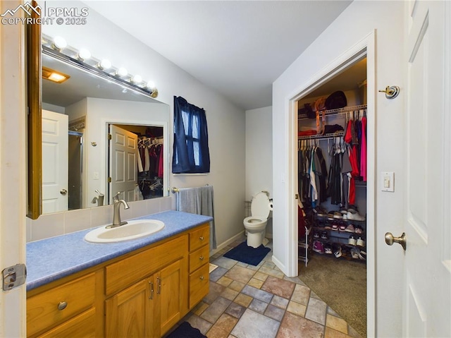 bathroom featuring toilet, a shower with shower door, vanity, baseboards, and stone finish floor