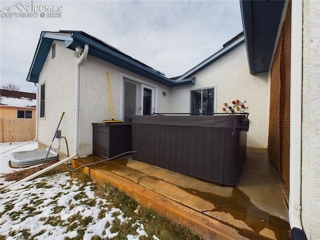 snow covered property with a hot tub and stucco siding