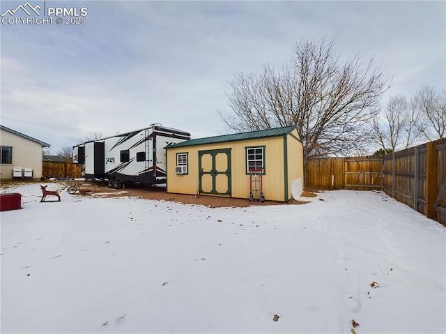 snow covered structure with a fenced backyard and an outbuilding