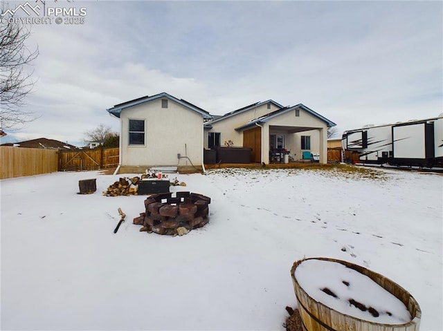 snow covered property featuring an outdoor fire pit, fence, and stucco siding