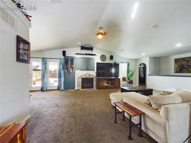 carpeted living area with lofted ceiling, visible vents, arched walkways, and a tiled fireplace