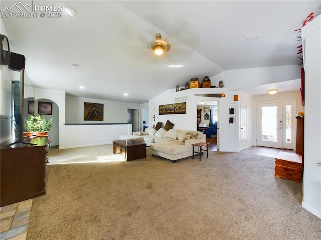 living area featuring lofted ceiling, baseboards, arched walkways, and light colored carpet