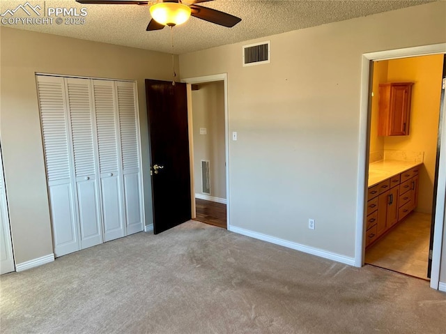 unfurnished bedroom featuring light carpet, a textured ceiling, a closet, and ceiling fan