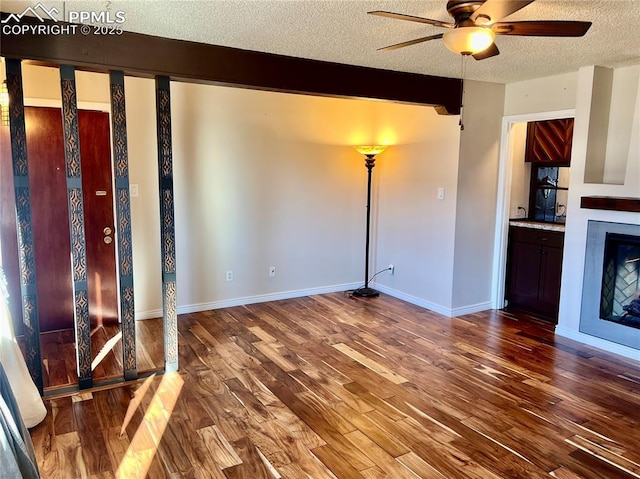 unfurnished living room with ceiling fan, wood-type flooring, beam ceiling, and a textured ceiling