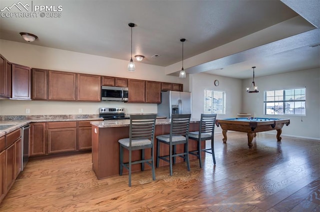 kitchen with light hardwood / wood-style flooring, hanging light fixtures, a kitchen breakfast bar, stainless steel appliances, and a center island