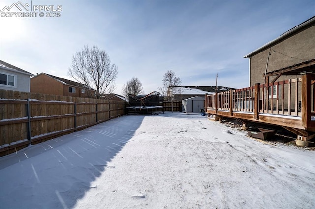 yard covered in snow featuring a trampoline, a storage shed, and a wooden deck