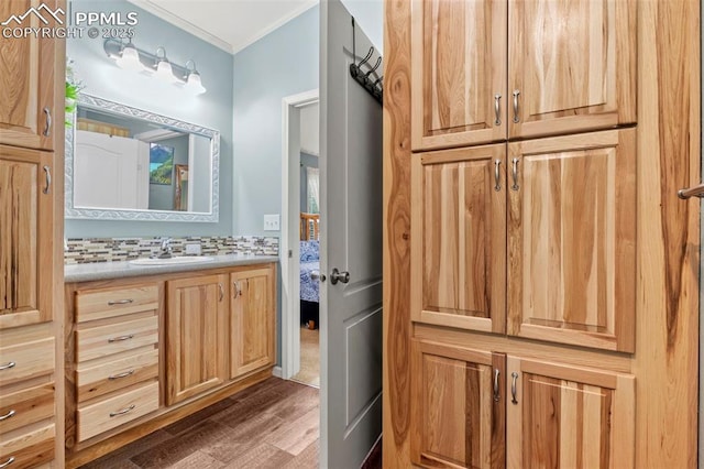 bathroom with vanity, wood-type flooring, crown molding, and decorative backsplash