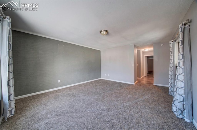 carpeted empty room featuring brick wall