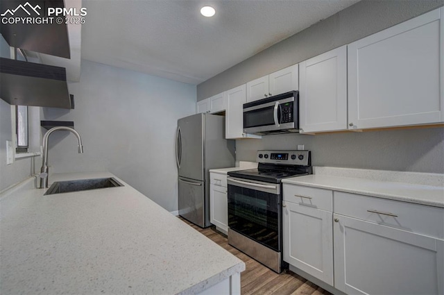 kitchen with sink, stainless steel appliances, white cabinets, and light wood-type flooring