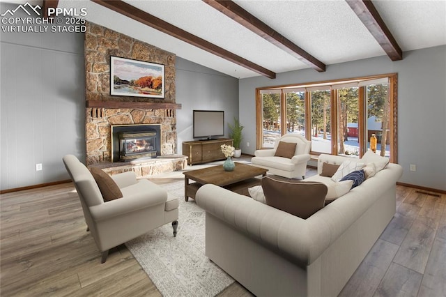 living room with a stone fireplace, vaulted ceiling with beams, a textured ceiling, and light hardwood / wood-style flooring