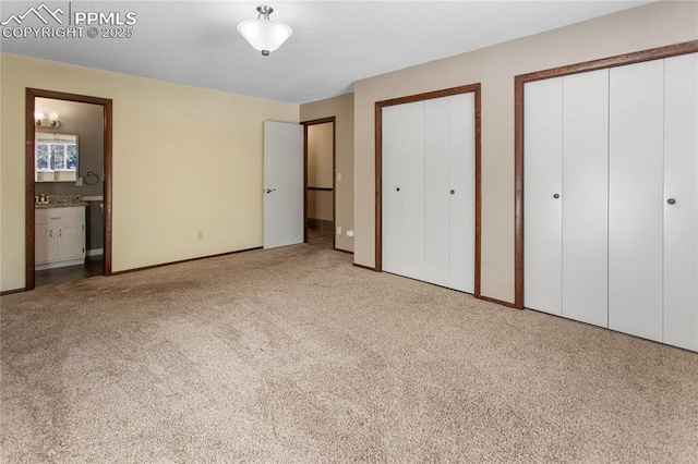 unfurnished bedroom with ensuite bathroom, carpet, and two closets