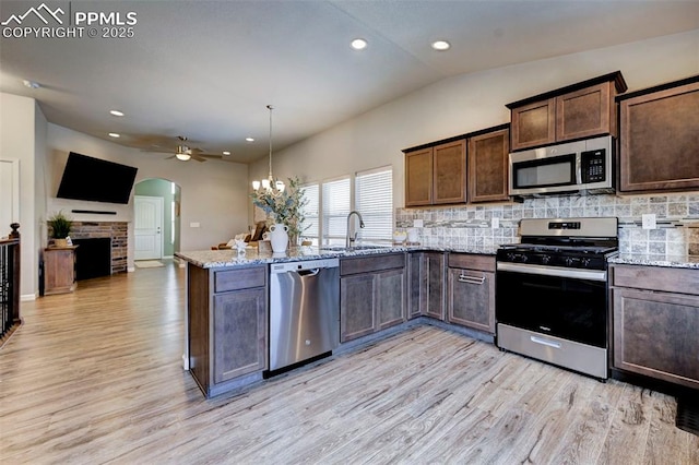 kitchen featuring appliances with stainless steel finishes, lofted ceiling, sink, hanging light fixtures, and light stone countertops