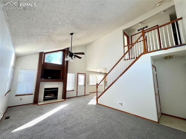 unfurnished living room with ceiling fan, carpet flooring, high vaulted ceiling, and a tile fireplace