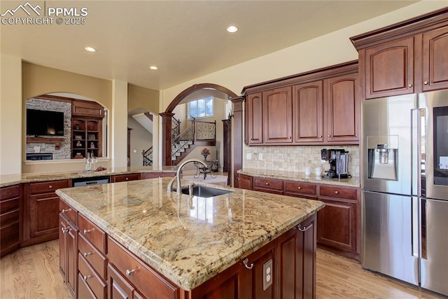 kitchen with sink, stainless steel fridge, a kitchen island with sink, light stone counters, and light hardwood / wood-style floors