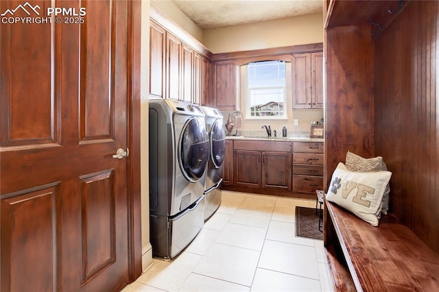 clothes washing area with cabinets, washing machine and dryer, and light tile patterned floors