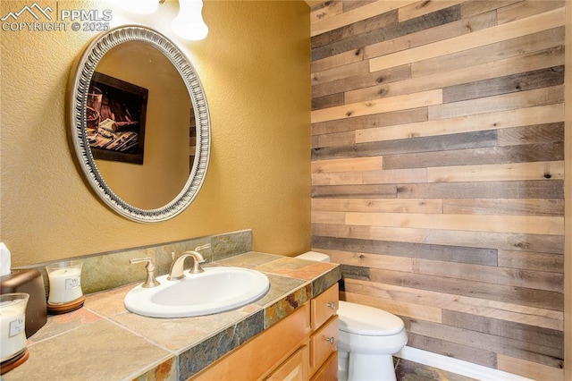 bathroom featuring vanity, toilet, and wood walls