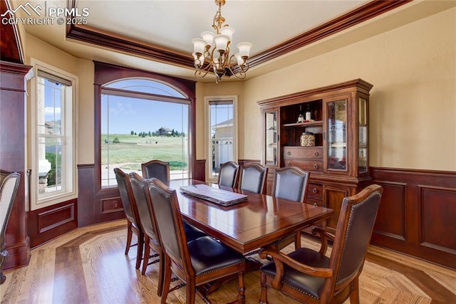 dining area featuring a raised ceiling, ornamental molding, a chandelier, and light hardwood / wood-style floors